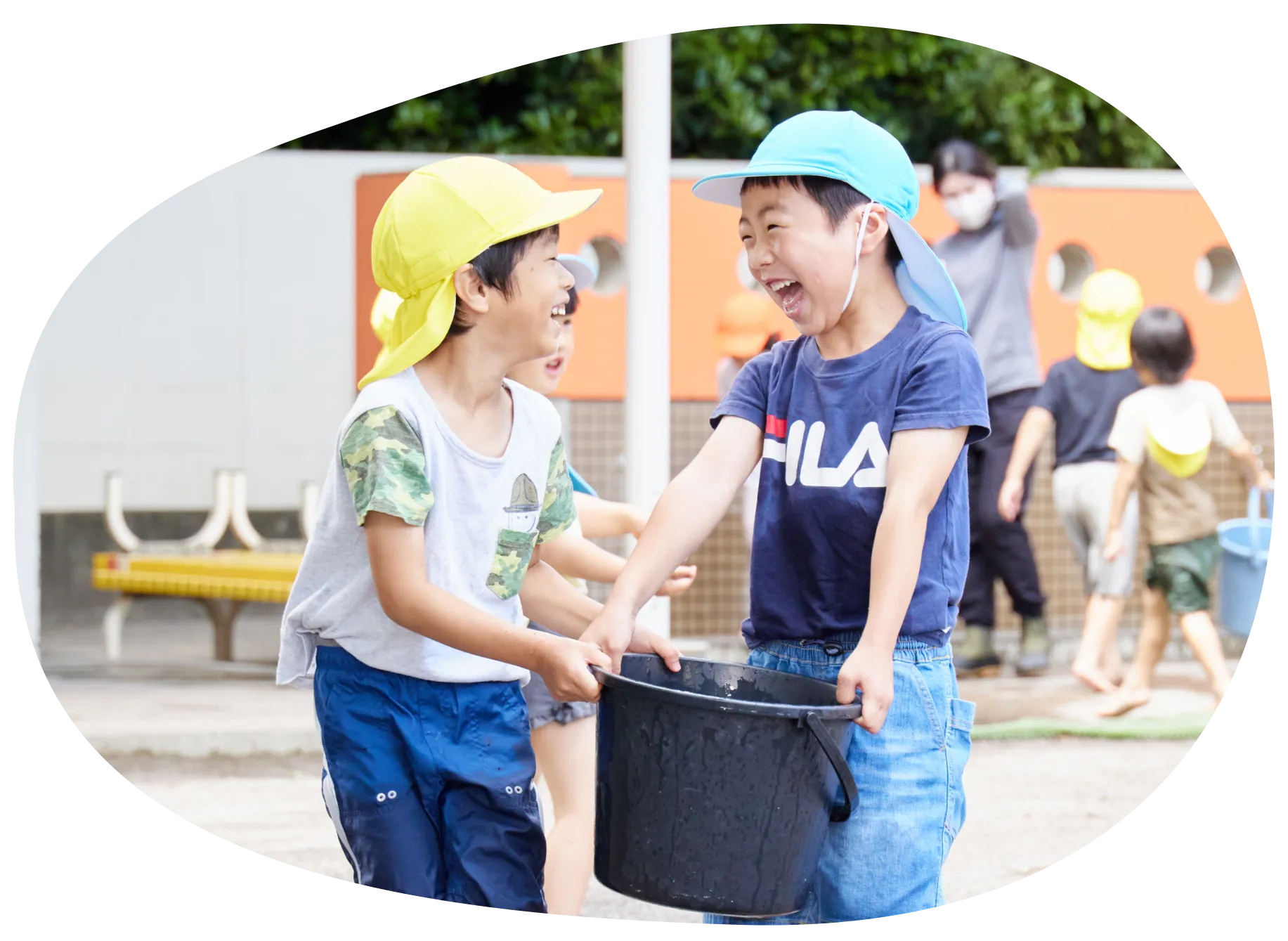 水の入ったバケツを運びながら笑い合う園児たち